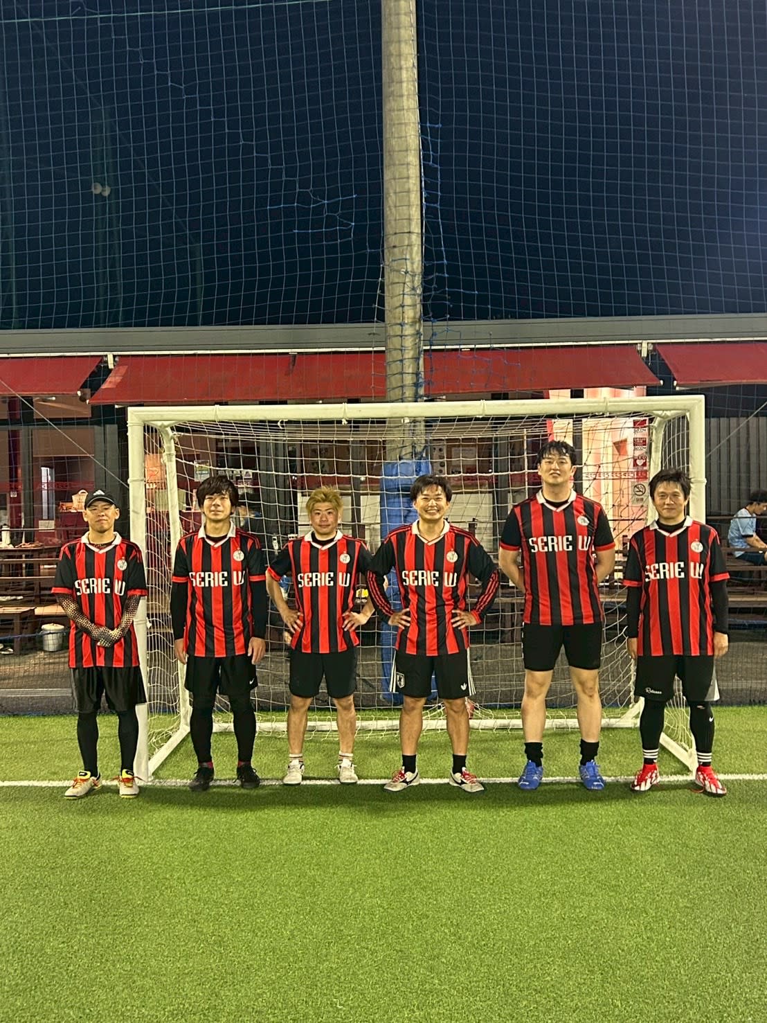 赤黒のSERIE Wユニフォームを着てフットサルゴール前に並ぶ大会メンバー6名