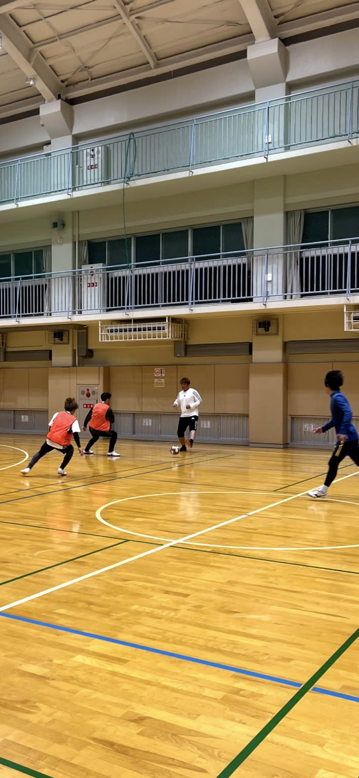 体育館のコートでビブスを着けた参加者たちがフットサルを楽しんでいる様子