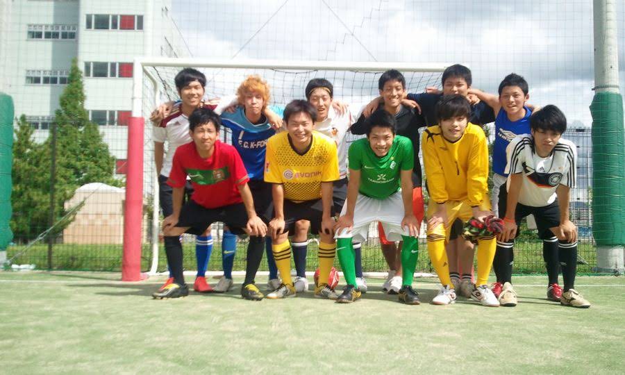 屋外フットサルコートのゴール前で並ぶ、昔のフットサル仲間たちの集合写真