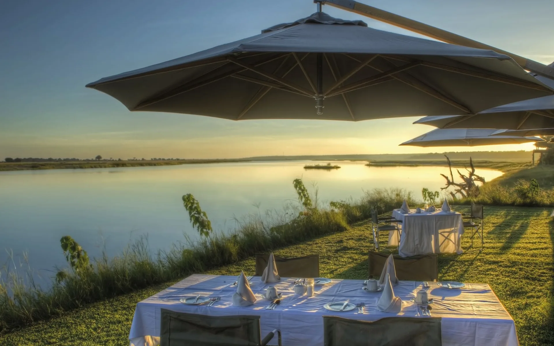 Chobe Game Lodge in Chobe Nationalpark: fb Chobe Game Lodge - Terrasse mit Esstisch und Sonnenuntergang am Fluss c Desert&Delta Safaris