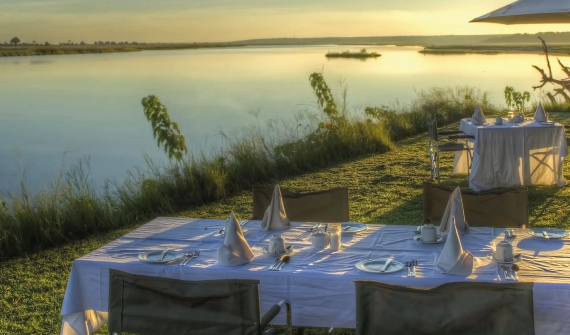 Chobe Game Lodge in Chobe Nationalpark: fb Chobe Game Lodge - Terrasse mit Esstisch und Sonnenuntergang am Fluss c Desert&Delta Safaris