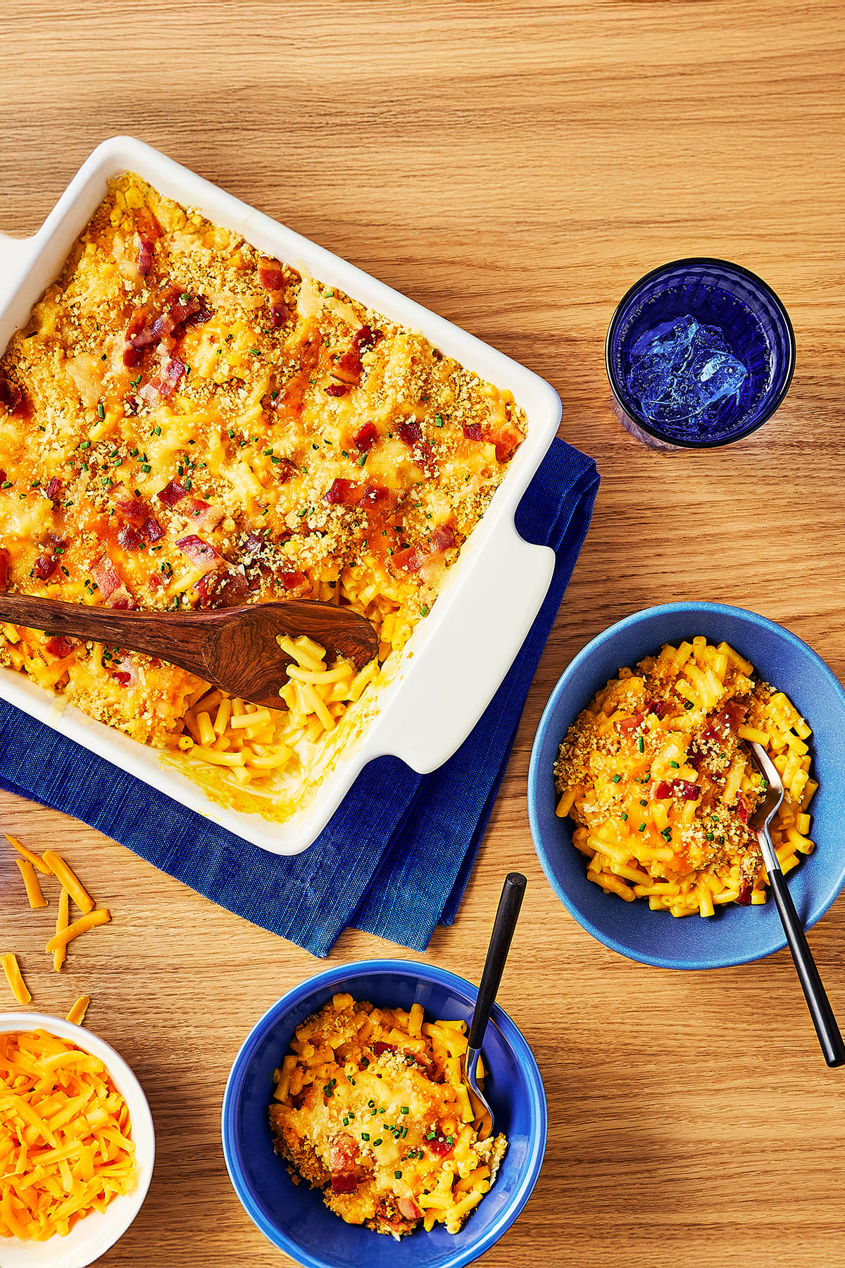 A rectangular baking dish filled with baked mac and cheese, topped with crispy bacon, breadcrumbs, and fresh chives. 