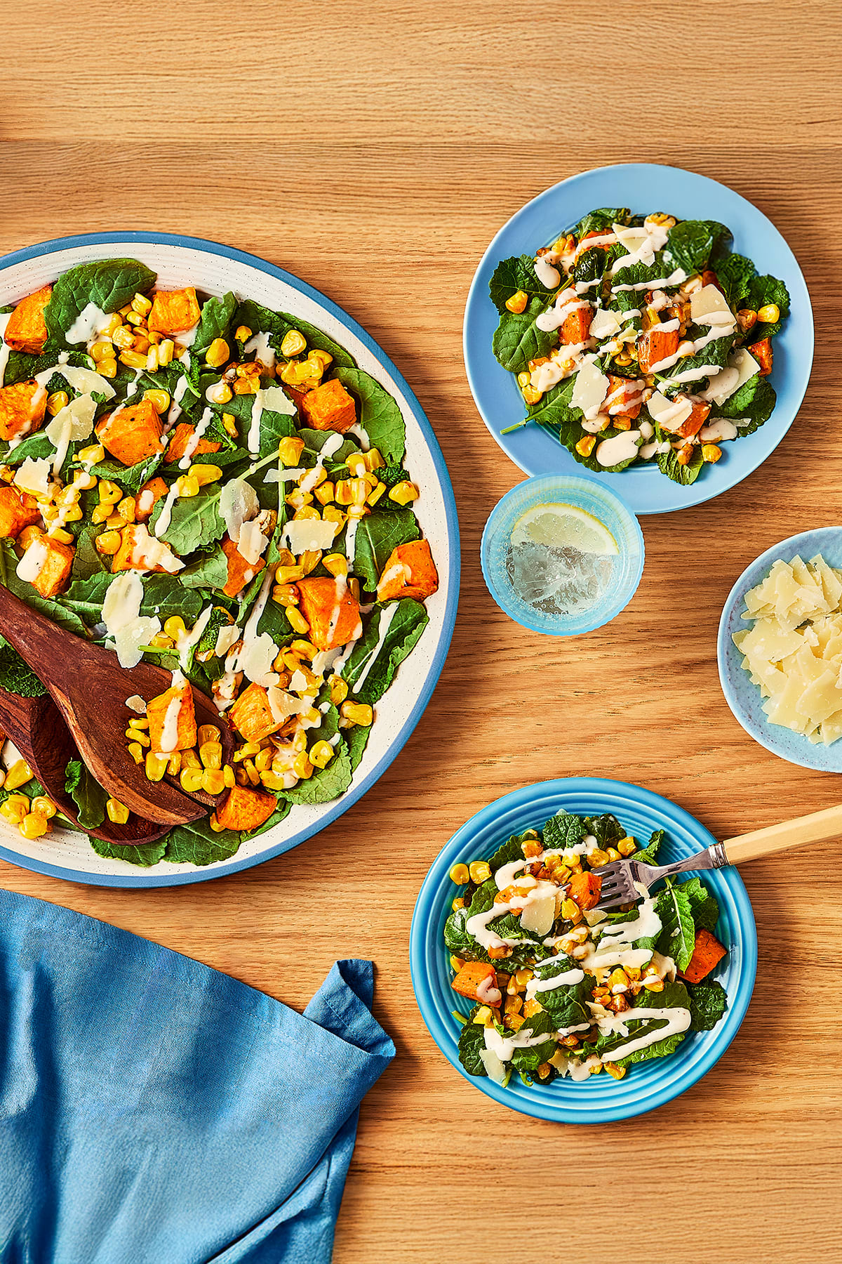 An overhead shot captures a salad, featuring roasted sweet potatoes, corn kernels, and fresh kale, drizzled with a dressing.