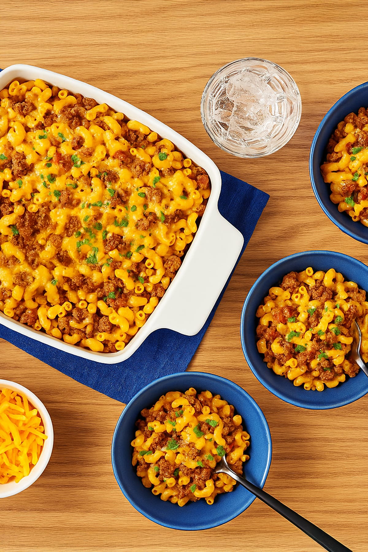 A white baking dish filled with macaroni, seasoned ground beef, and melted cheese, garnished with chopped parsley.