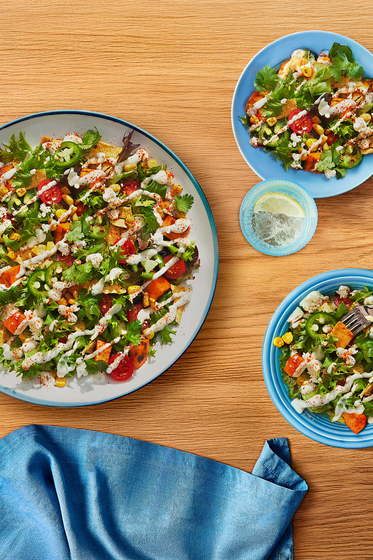 Trois bols bleus salade patates douces rôties, maïs, tomates, jalapeños, fromage, coriandre. Vinaigrette crémeuse, épices.