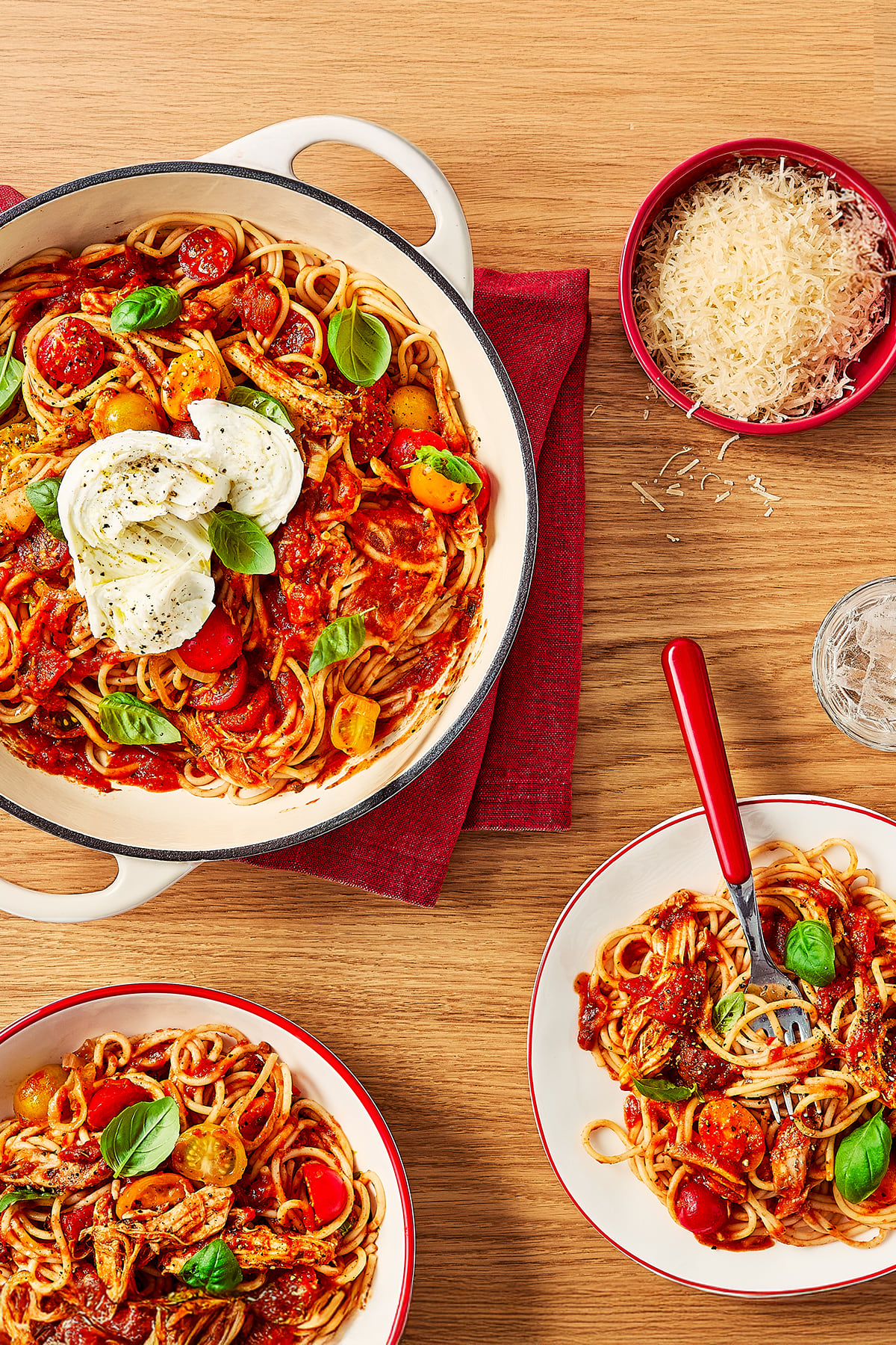 A serving pan is filled with spaghetti tossed in a tomato sauce with cherry tomatoes, pulled chicken, and fresh basil. 