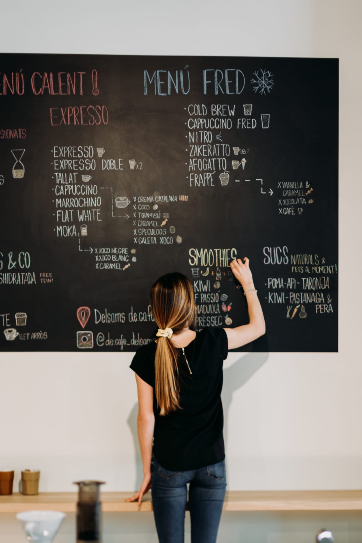 A woman writes on a coffee shop black board.