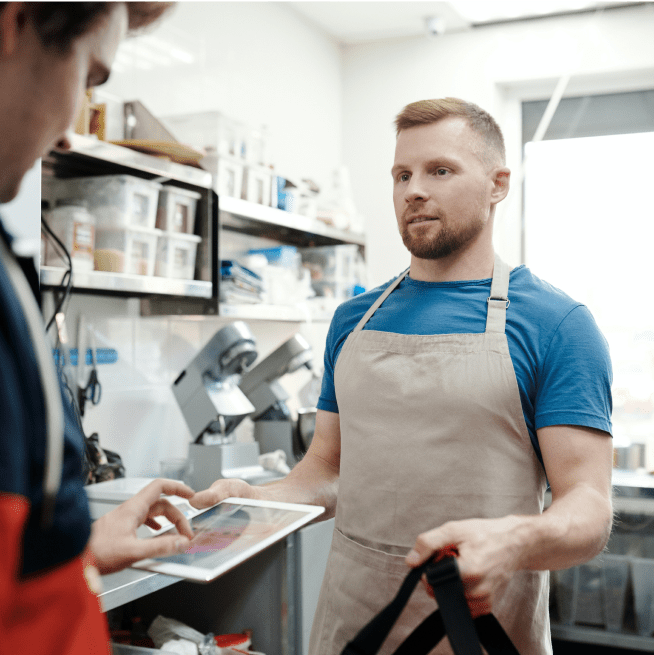 Man in an apron standing in a kitchen holding an Ipad