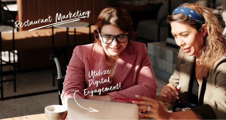 Two women having a meeting sitting down at a table looking at a laptop in a coffee shop.