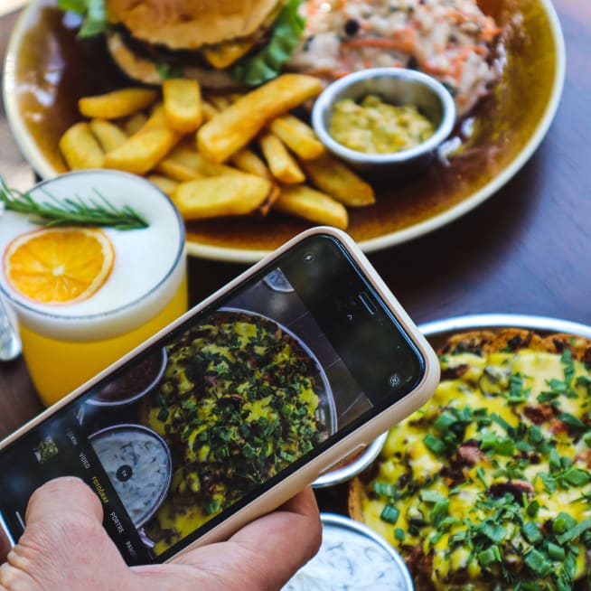 Hand holding a cellphone taking a photo of their meal