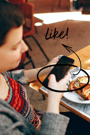 A person sitting at a patio table outside with food and using a cellphone