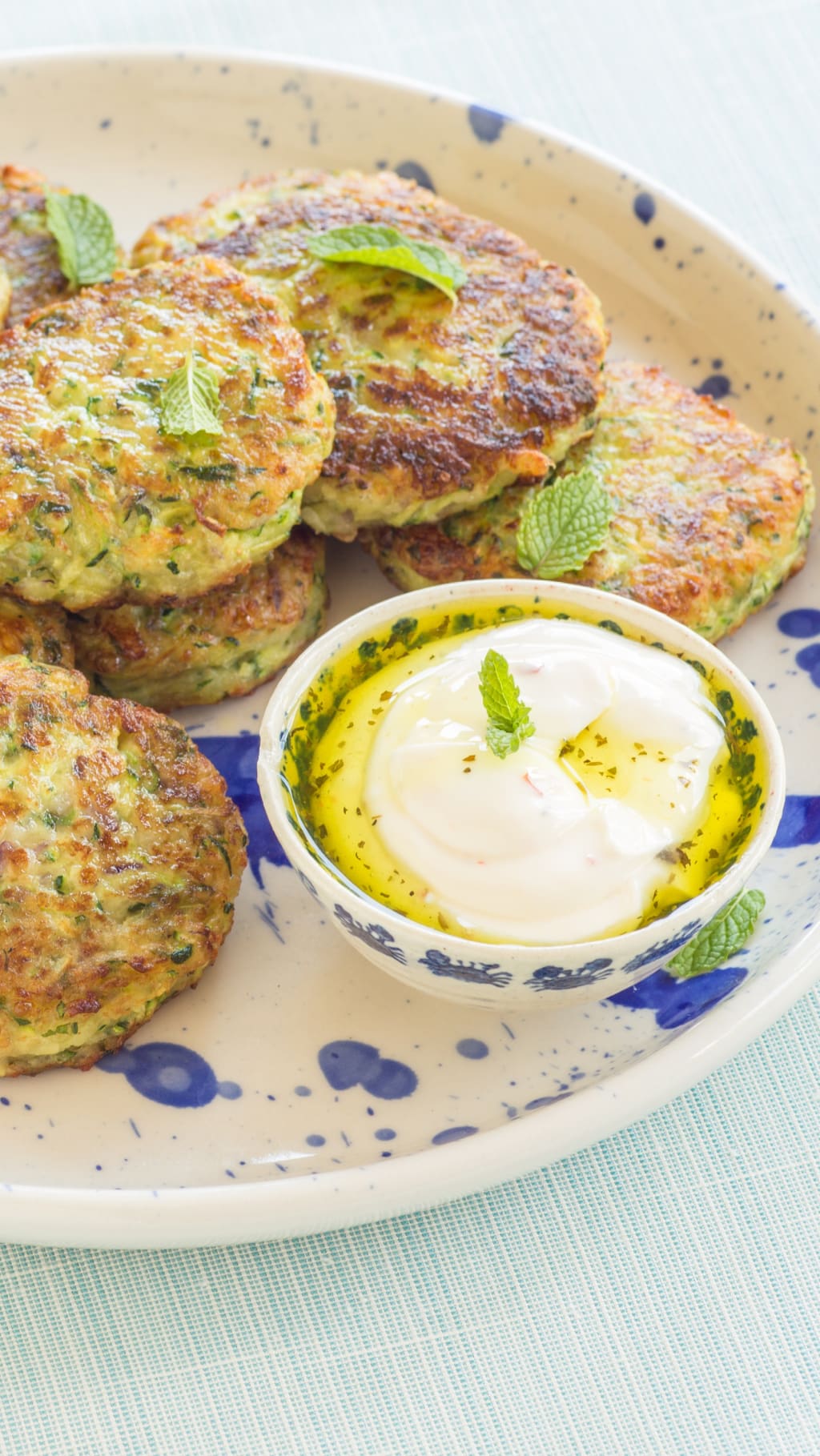 Herby fritters and a small bowl of dipping sauce on a blue speckled plate.