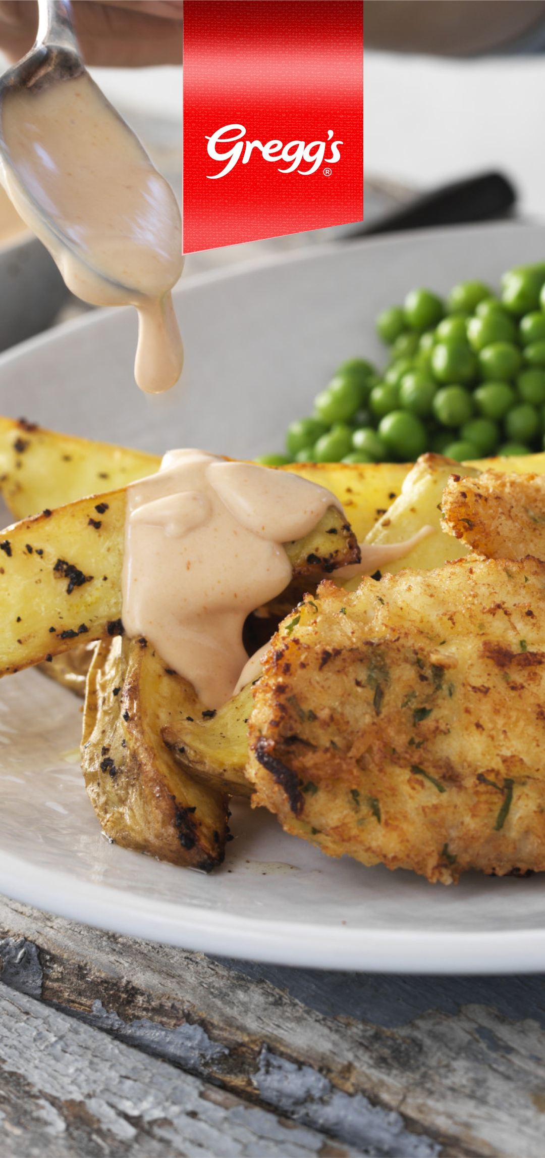 A spoon drizzling a creamy sauce over a plate of chicken, potatoes, and peas.