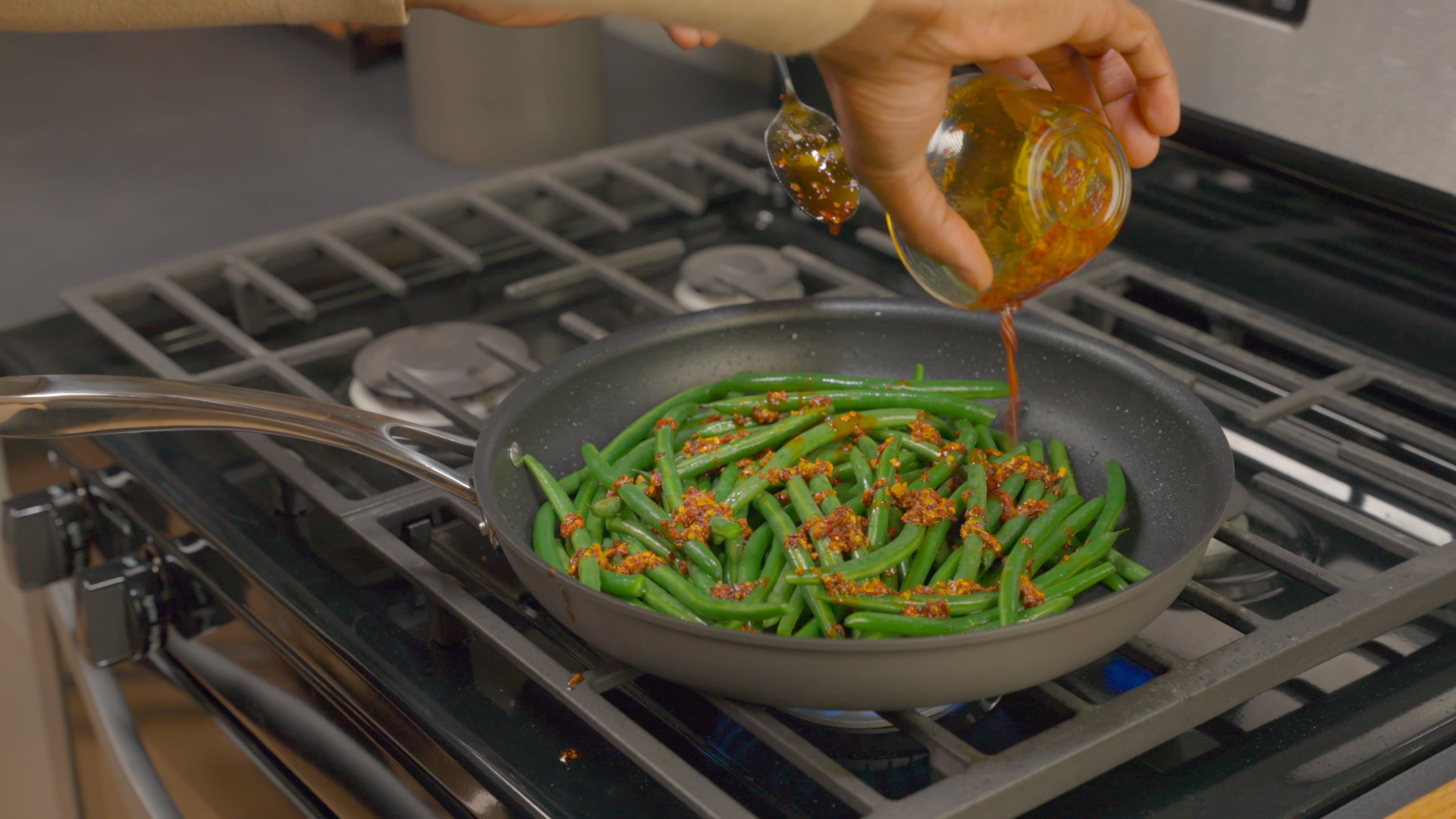 Heinz Chili Pepper Crunch Sauce being poured over green beans and mixed.