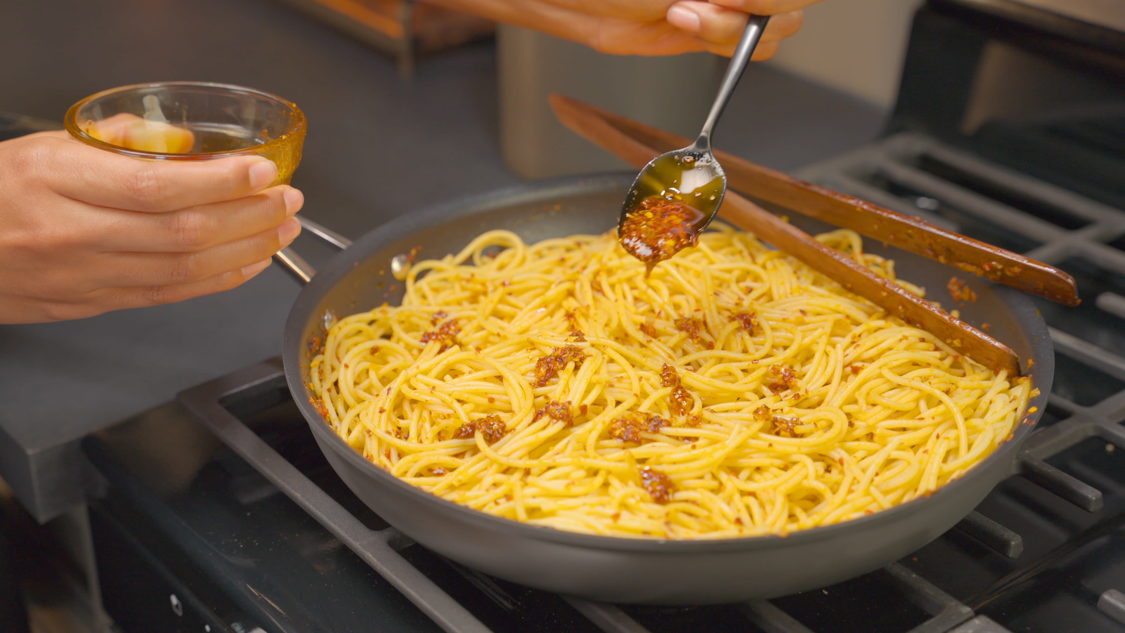 Cooked spaghetti in the pan being drizzled with Heinz Chili Pepper Crunch Sauce.