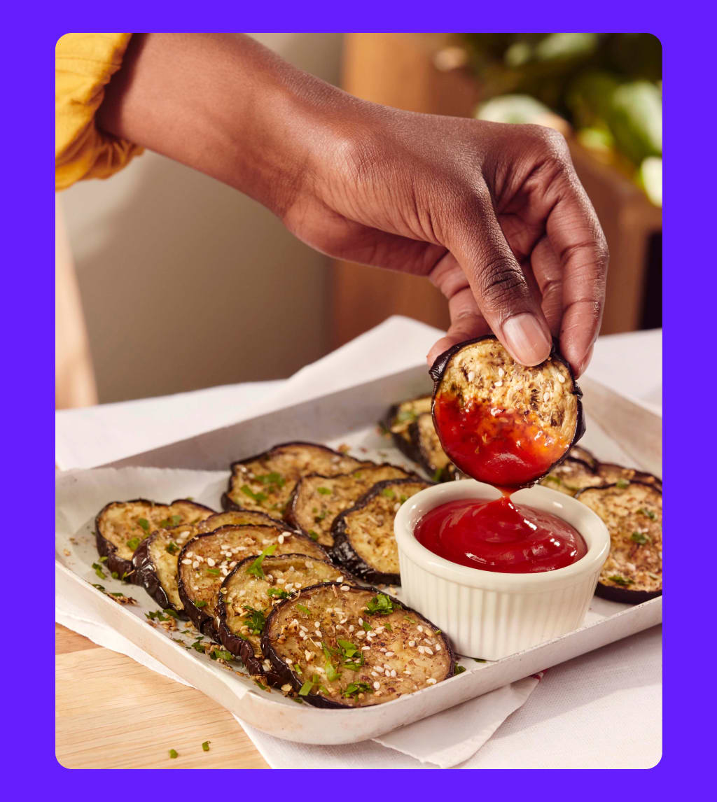 Foto van een hand die een aubergine in de ketchup doopt.