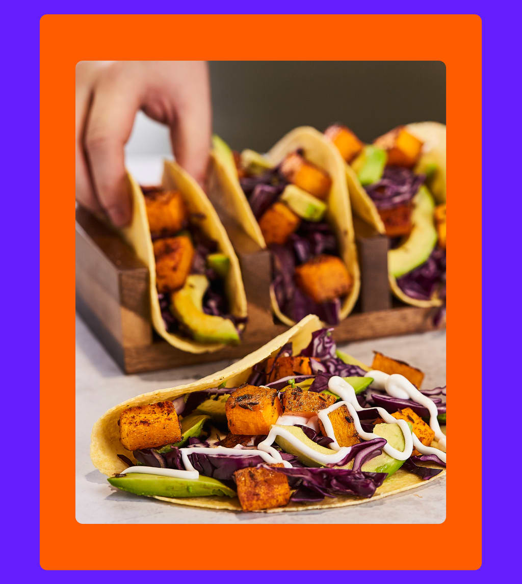 Primo piano di tacos vegani con zucca butternut grigliata, avocado e cavolo rosso.