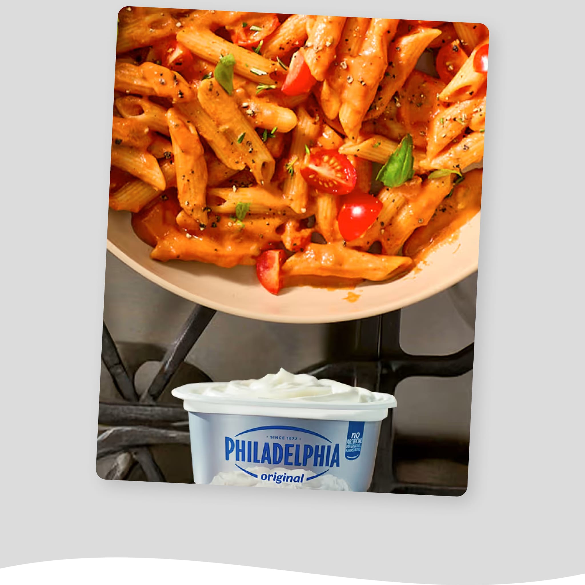 Close-up of a skillet filled with penne pasta in a creamy tomato sauce, topped with fresh basil and halved cherry tomatoes. 