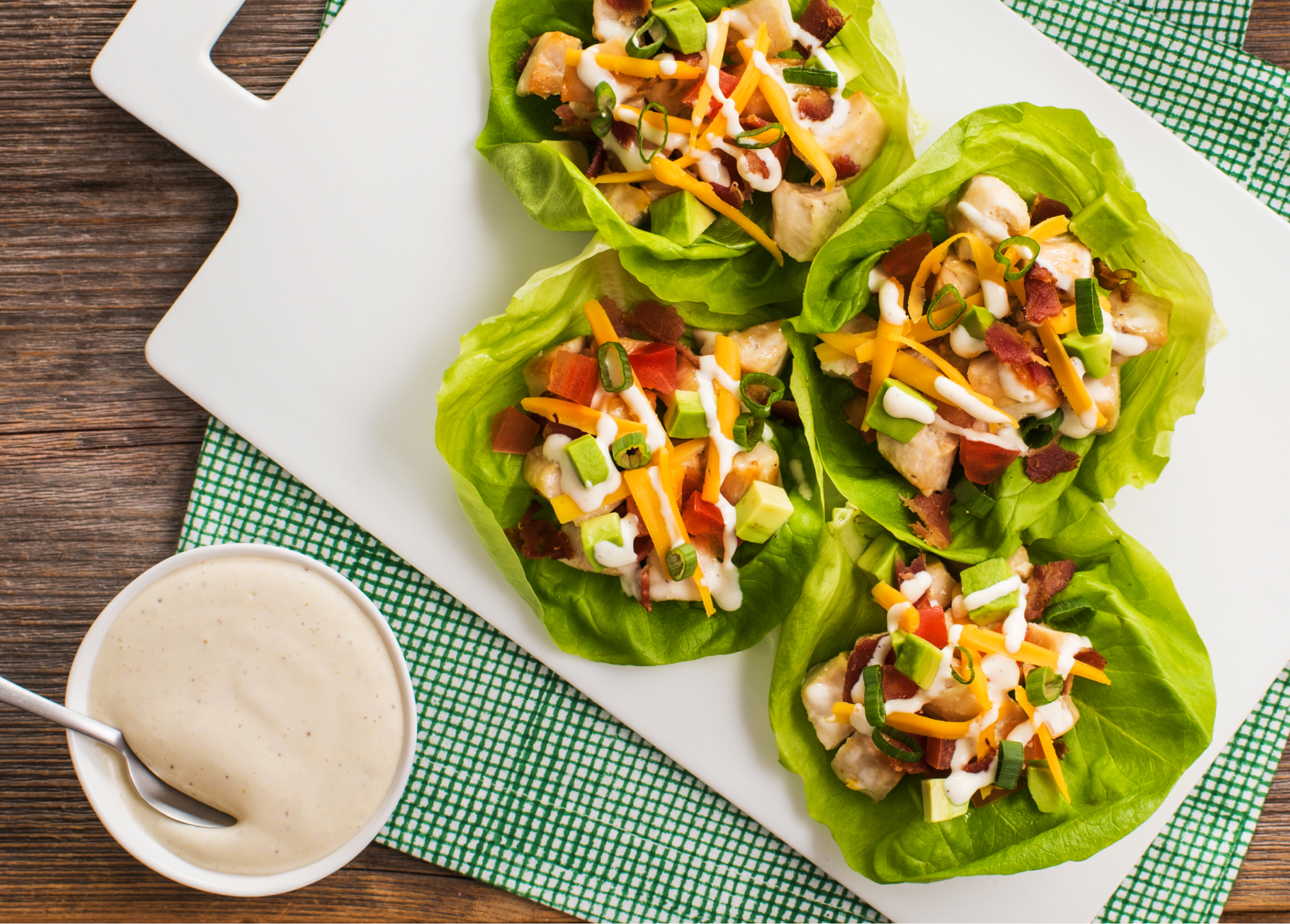 Lettuce wraps with chicken, bacon, cheese, avocado, and dressing on a white plate.