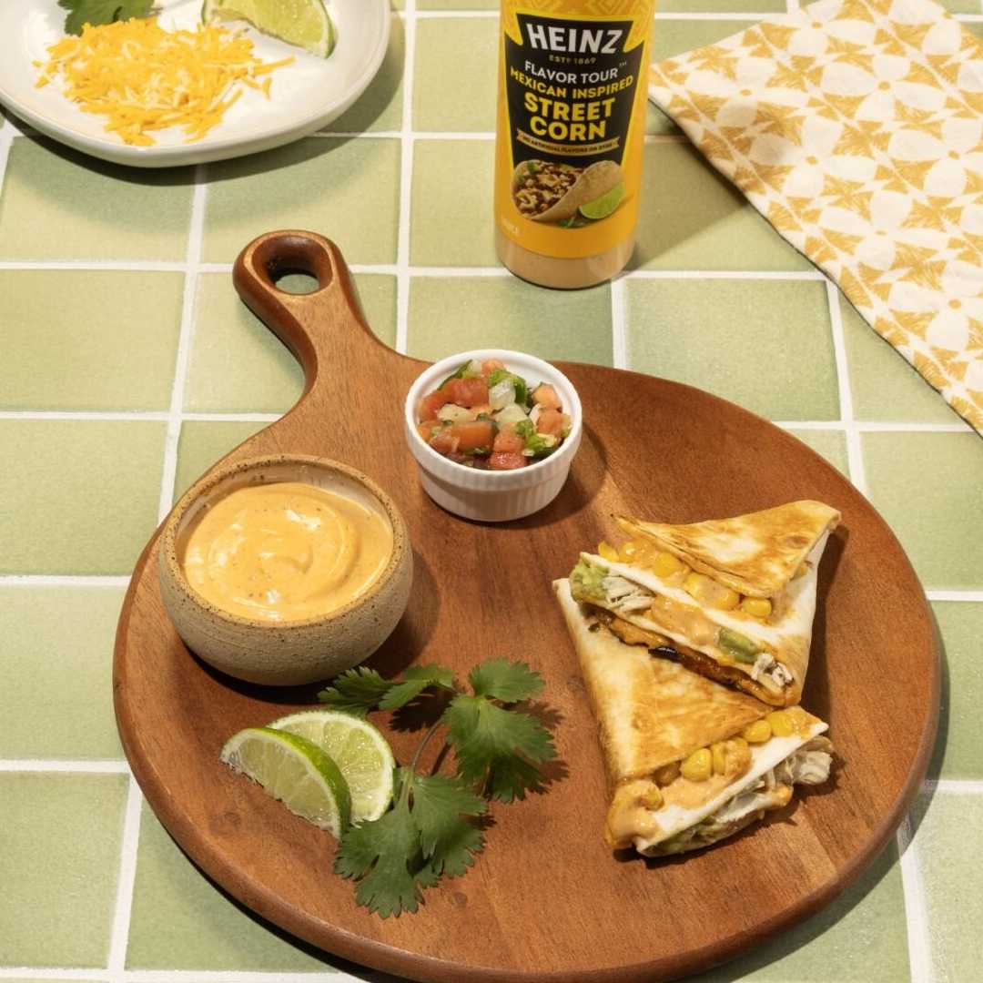 Two golden-brown quesadillas, filled with savory chicken, creamy avocado, and sweet corn, are presented on a rustic wooden se
