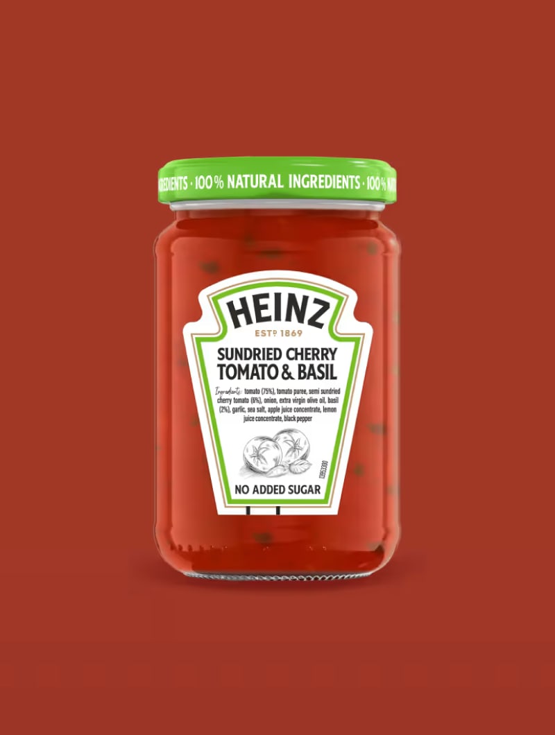  Et glas Heinz Sundried Cherry Tomato & Basil sauce, med "No Added Sugar" fremhævet, mod en levende grøn baggrund.