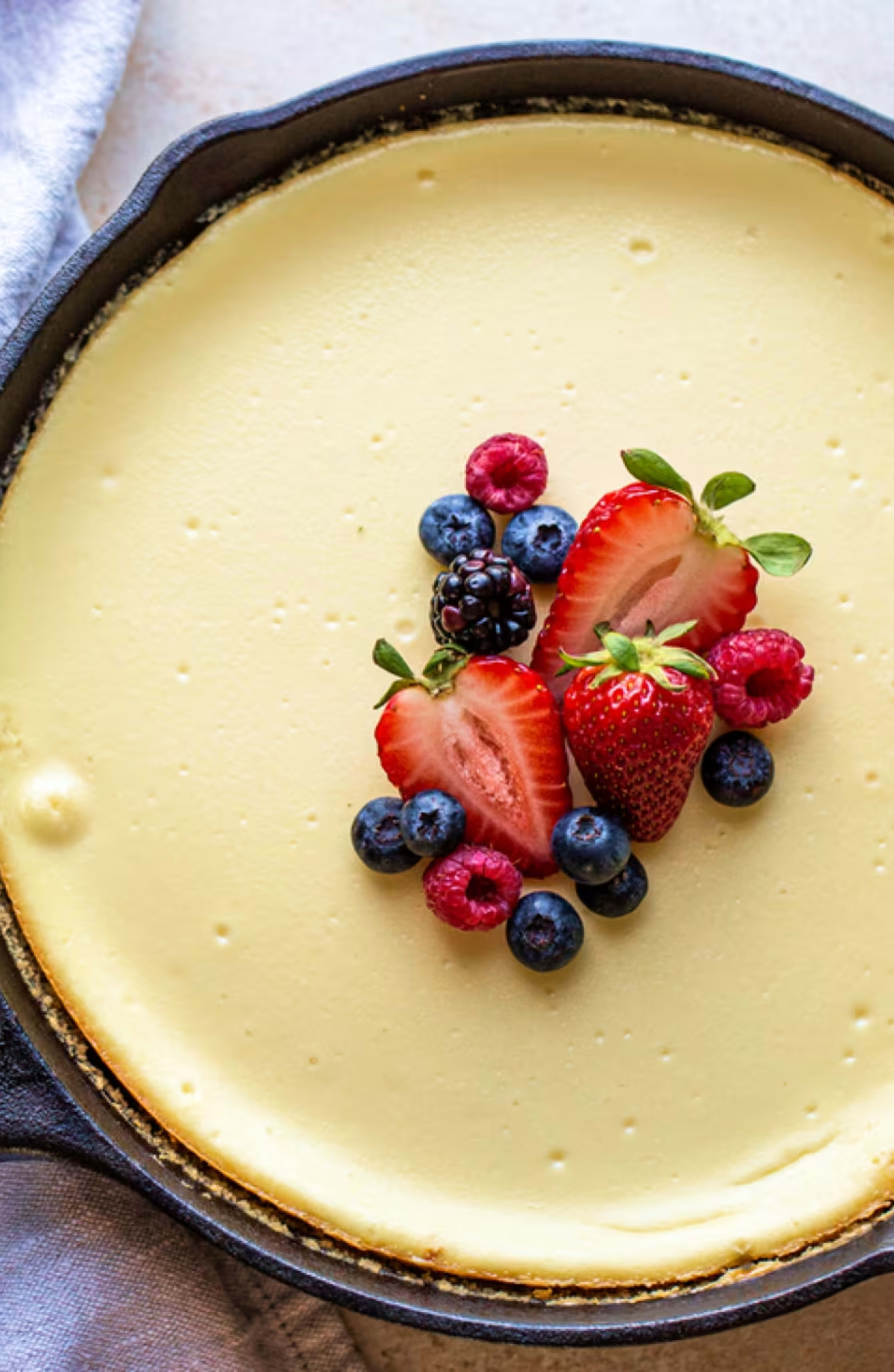 A delicious homemade cheesecake baked in a skillet, topped with fresh strawberries, blueberries, raspberries, and a blackberry. Made with Philadelphia Cream Cheese