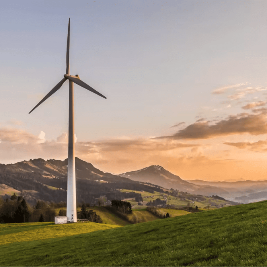 A wind turbine stands tall in a green field against a mountain backdrop at sunset