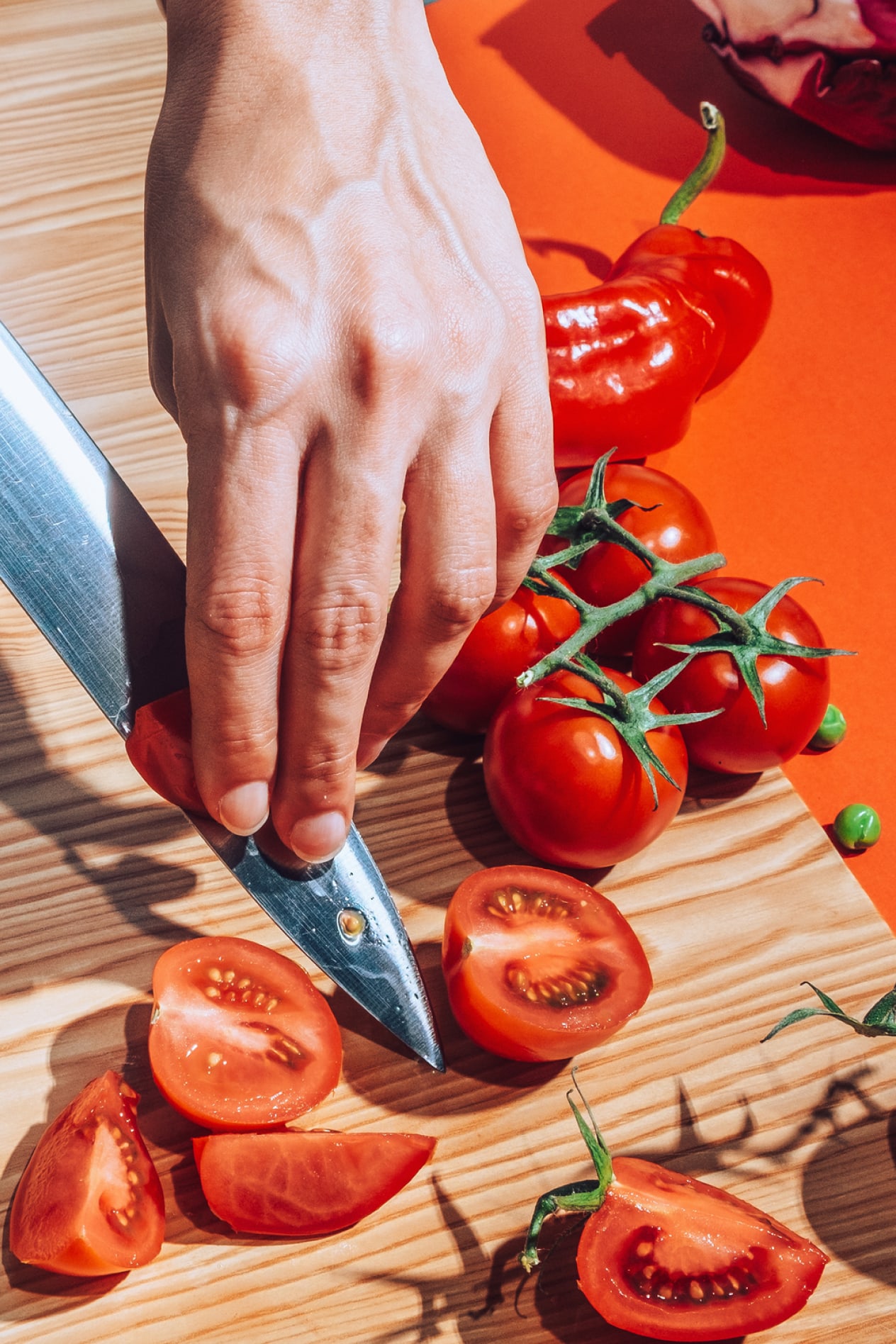 A man's hands chop cherry tomatoes.