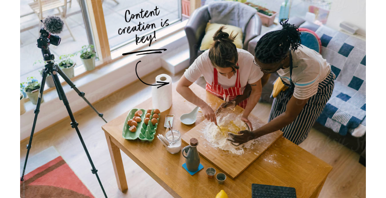Two people baking together, being filmed by a camera.