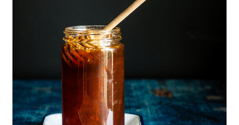 Honey jar with stick on a dark background.