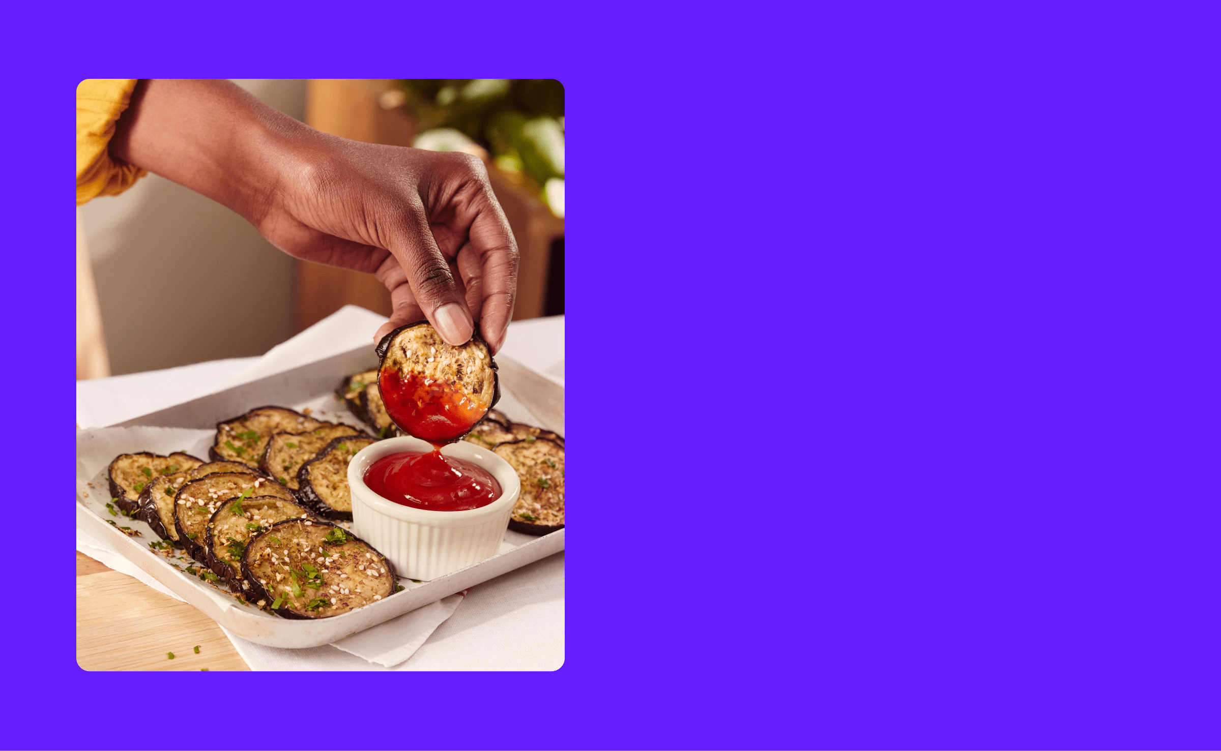 Foto van een hand die een aubergine in de ketchup doopt.