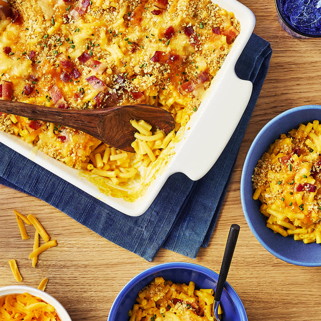 Overhead view of a cheesy macaroni casserole topped with bacon and chives next to individual servings.