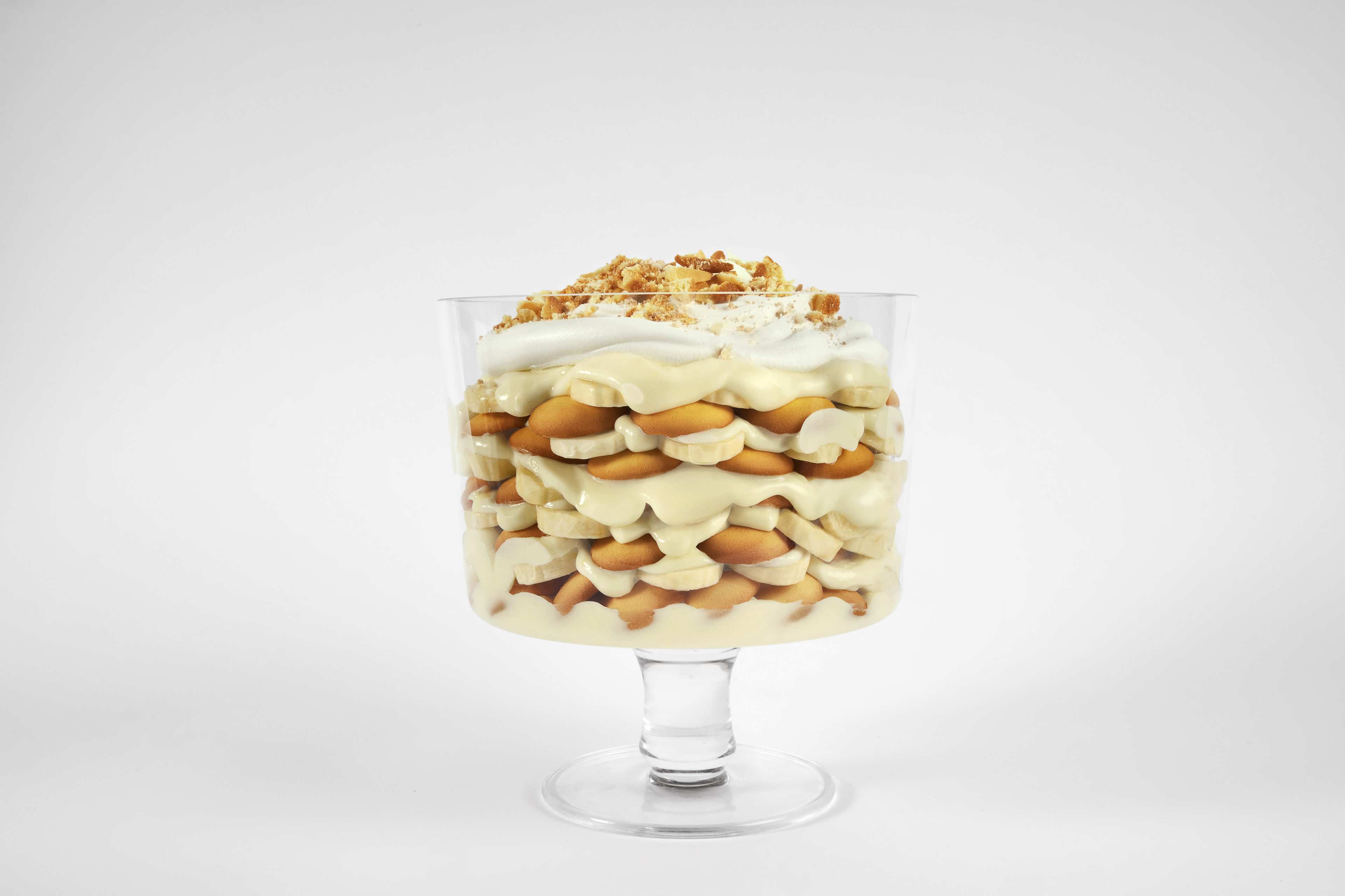 A trifle dish of layered banana pudding with vanilla wafers, sliced bananas, pudding, and crushed vanilla wafers on top.