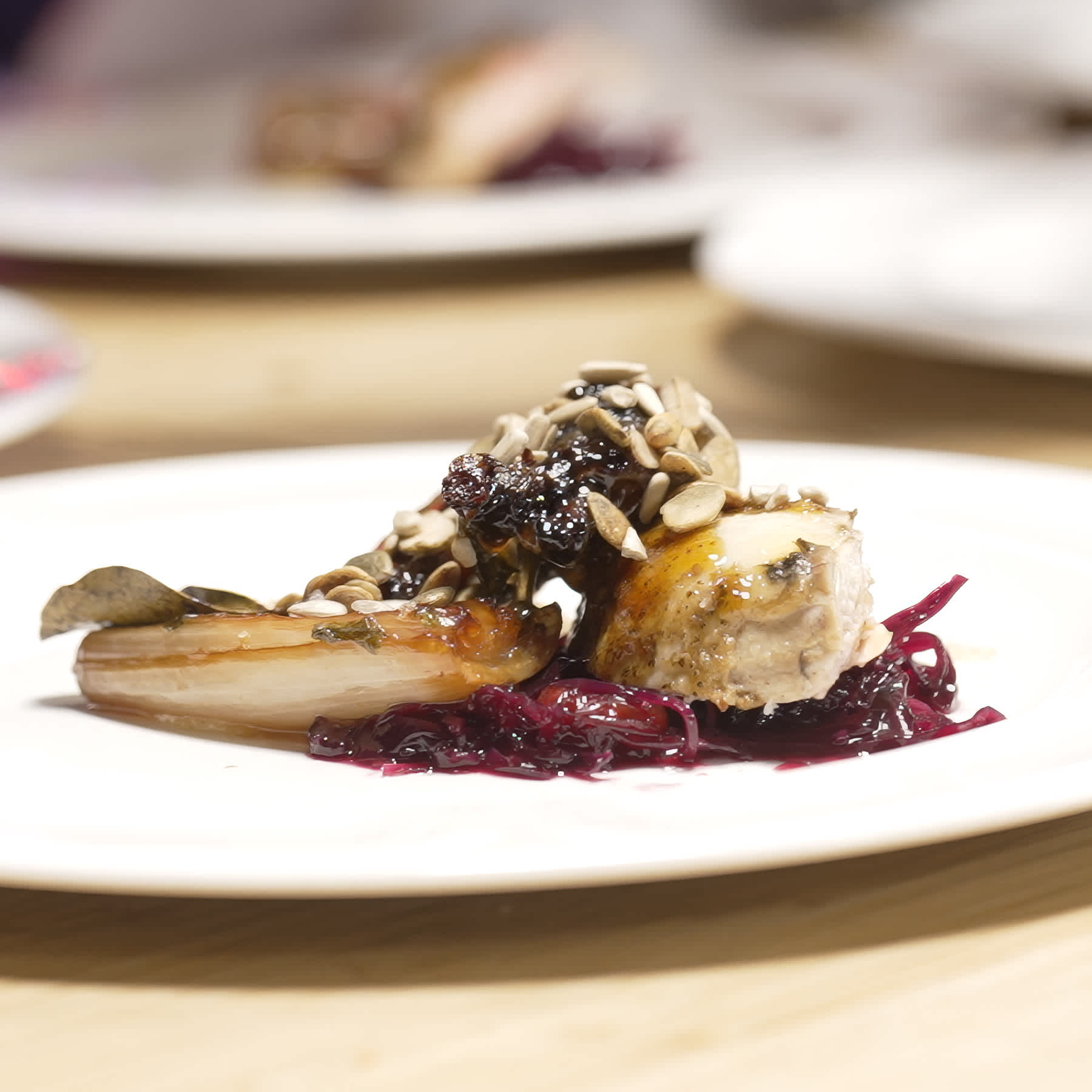 Roasted chicken and vegetables served on a bed of braised red cabbage, garnished with toasted sunflower seeds.