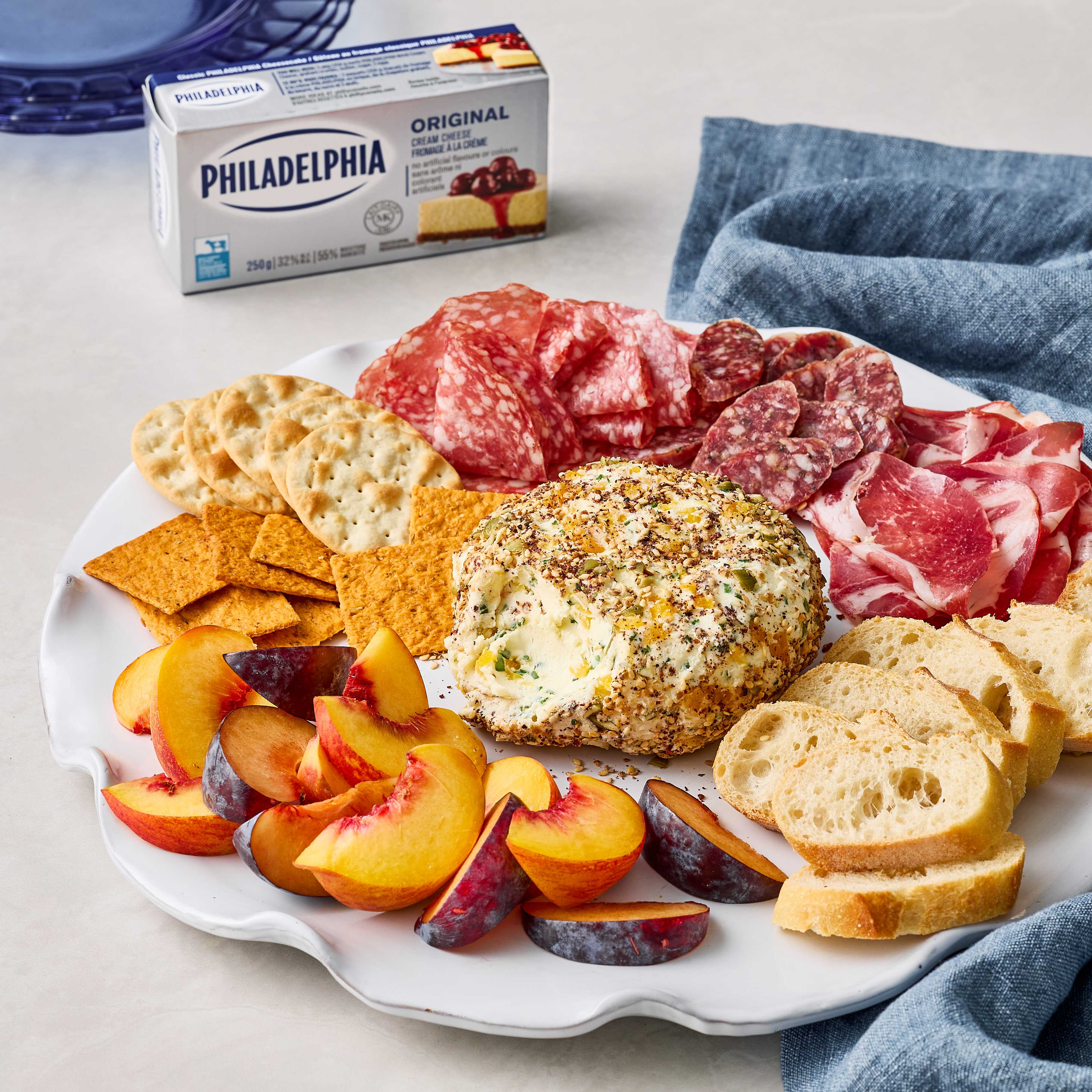 Seed and spice crusted Philadelphia cheese and apricot spread on a platter with salami, crackers, and fruit.