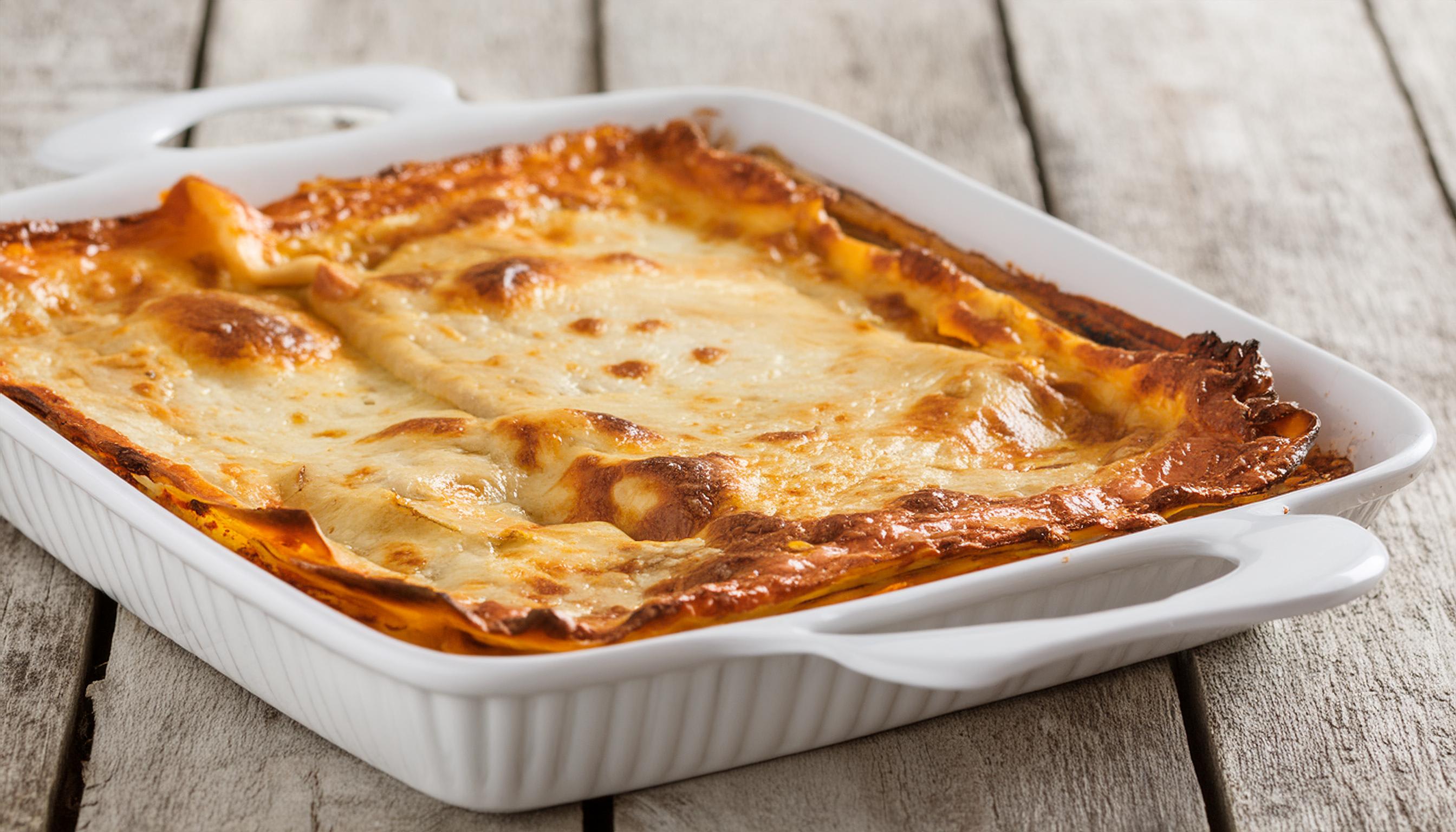 A square white baking dish filled with golden-brown, cheesy baked beef lasagne.