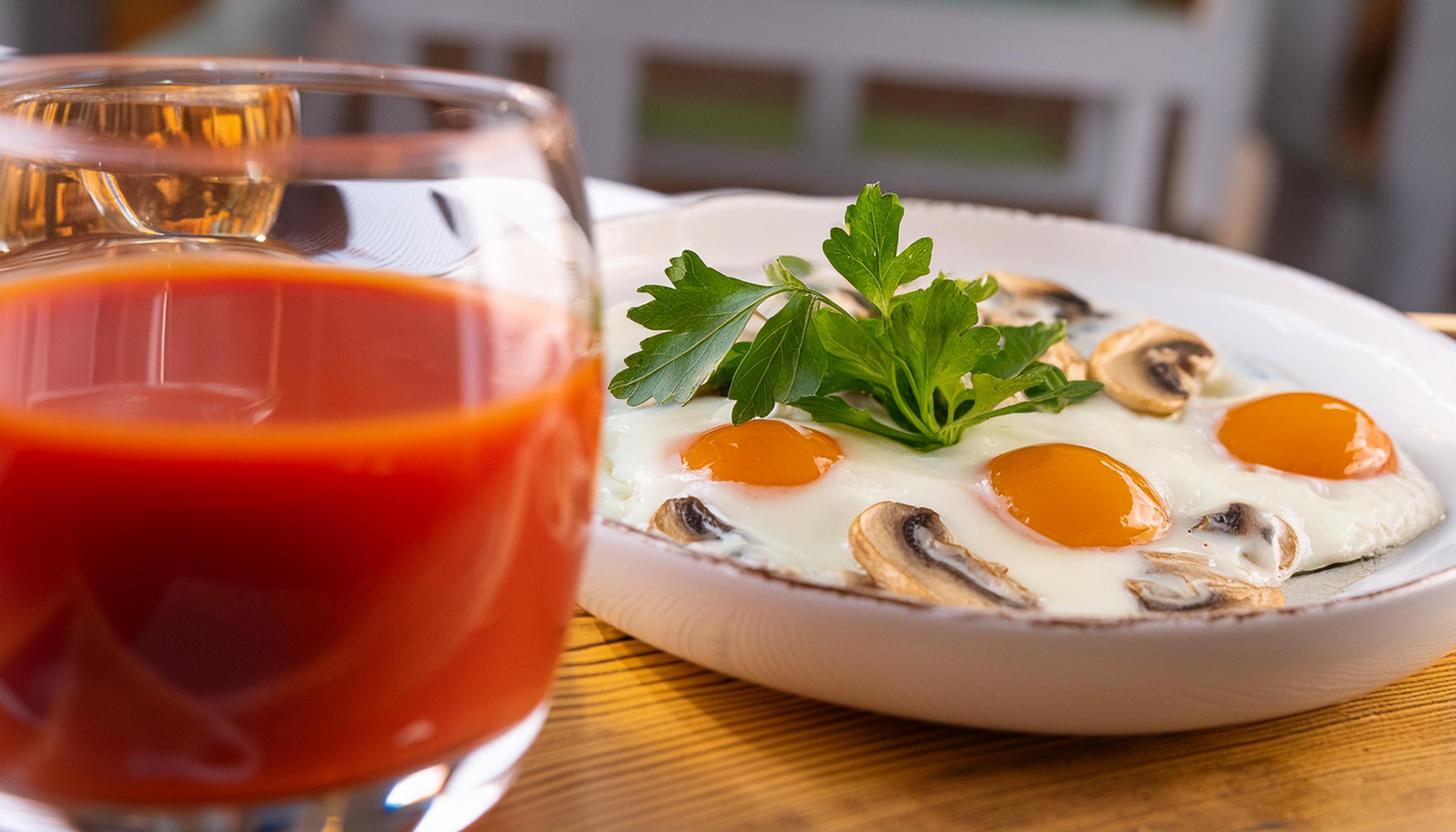 Sunny-side-up eggs with mushrooms and parsley next to a glass of tomato juice.