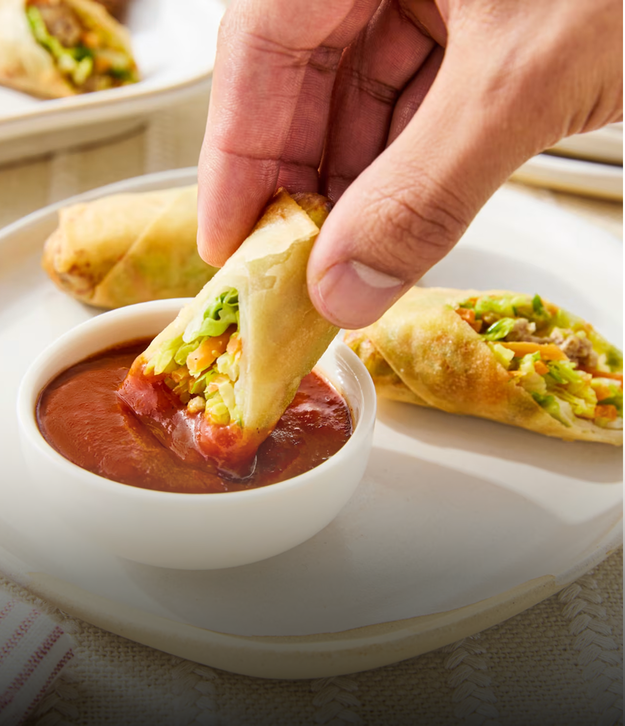 Une main trempe un rouleau de printemps croustillant, rempli de légumes frais, dans un bol de sauce chili Heinz.