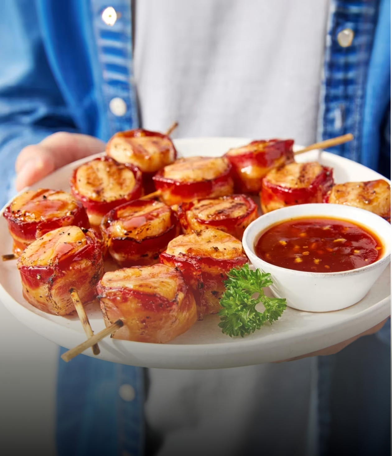Plate of bacon-wrapped scallops on skewers, served with a side of Heinz Chili Sauce.