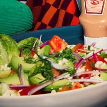 Fresh avocado, tomato, red onion, feta, and dill combine in a vibrant salad. Creamy dressing and a checkered napkin complete the scene, ideal for showcasing lunch recipes.