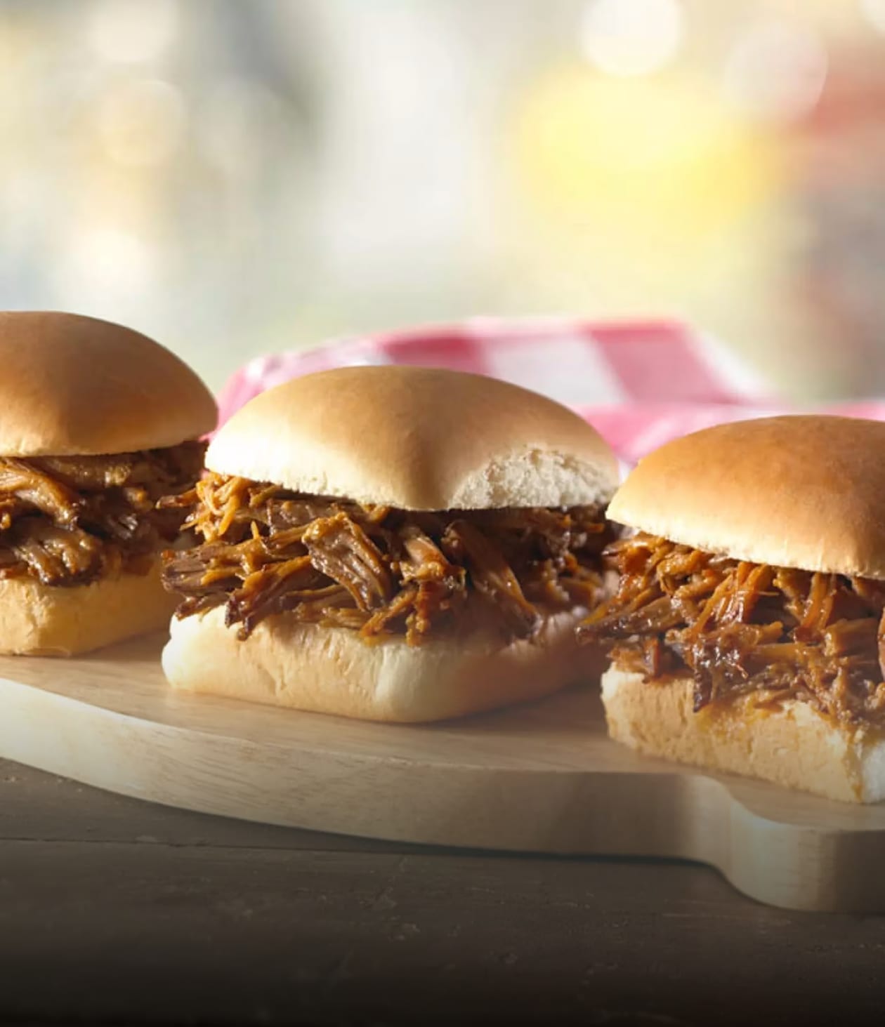 Trois délicieux mini-sandwichs au porc effiloché sur une planche en bois.