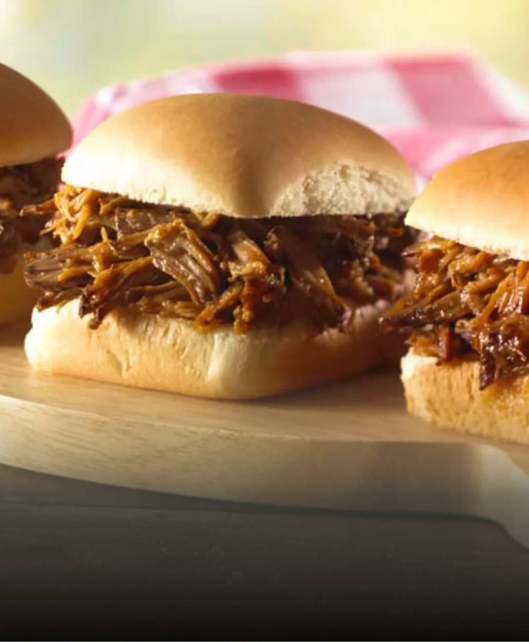 Deux mini-sandwichs au porc effiloché sur une planche à découper en bois, parfaits pour un pique-nique ou une fête.