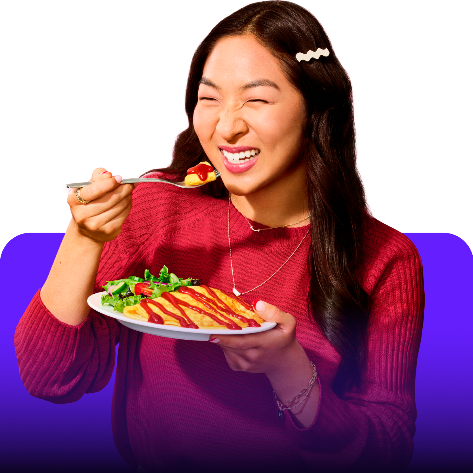 A girl smiles while holding a plate of omelette with ketchup and a forkful of omelette.