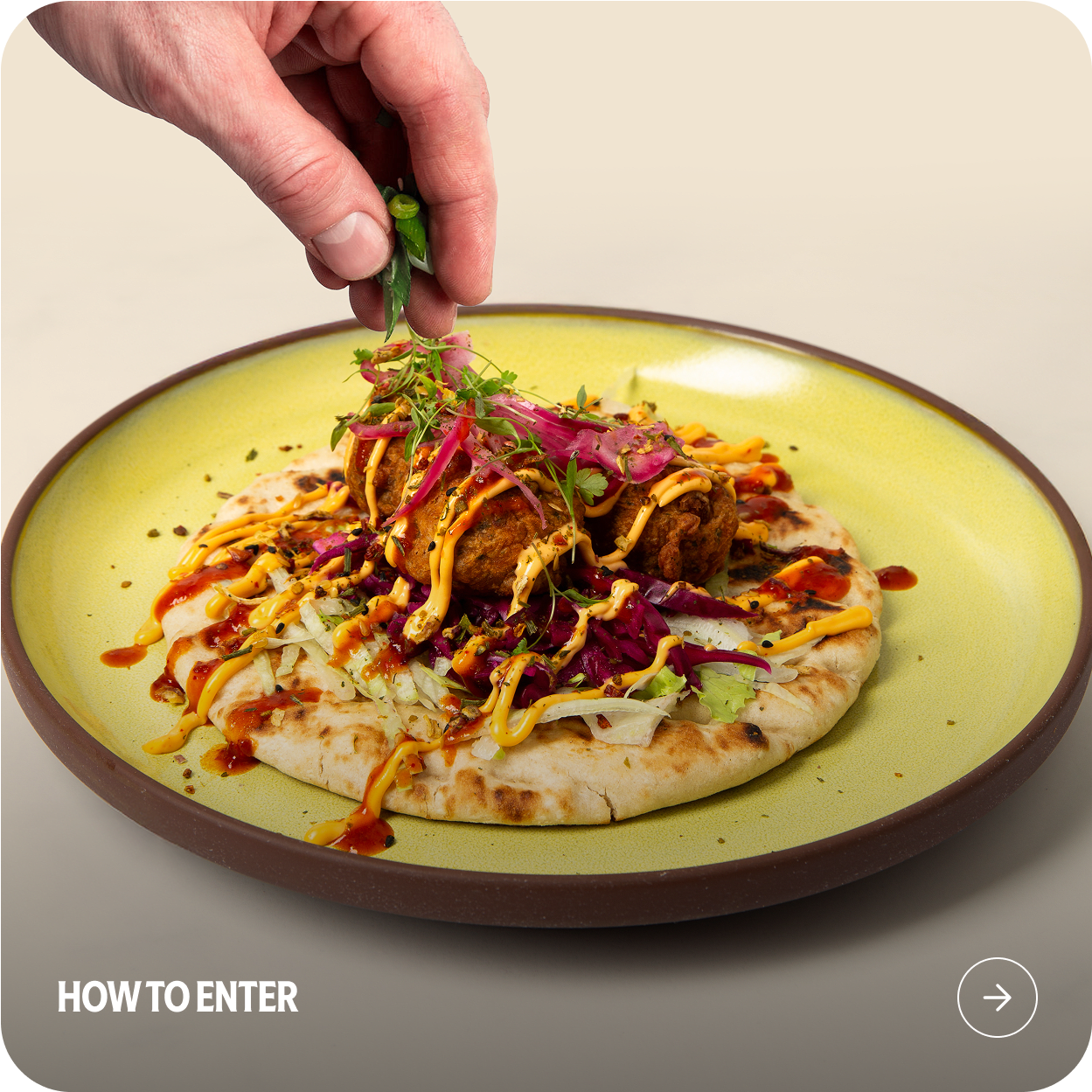 Close-up of a hand garnishing a vibrant falafel flatbread with fresh herbs. 