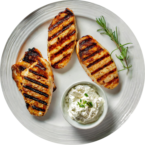 Overhead shot of a white plate with three grilled chicken breasts. The chicken has prominent grill marks and is slightly charred. A small bowl of creamy herb sauce sits on the side, and a sprig of rosemary garnishes the plate