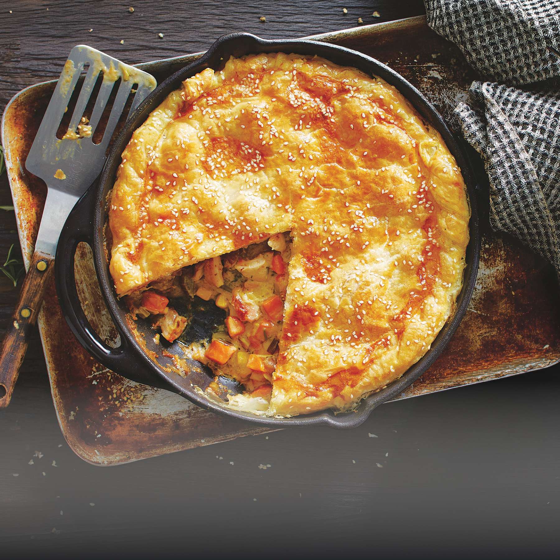 Golden-brown puff pastry chicken pot pie in a cast-iron skillet, sliced to show vegetable and chicken filling.