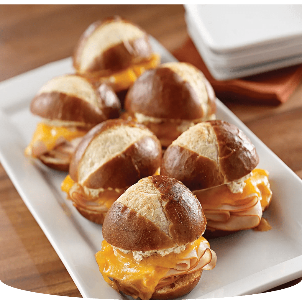 Mini sandwiches with ham, cheese, and pretzel buns on a white plate.