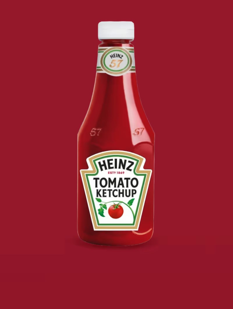 En klassisk glasflaske Heinz Tomat Ketchup med hvid etiket og et tomatbillede, sat mod en dybrød baggrund.