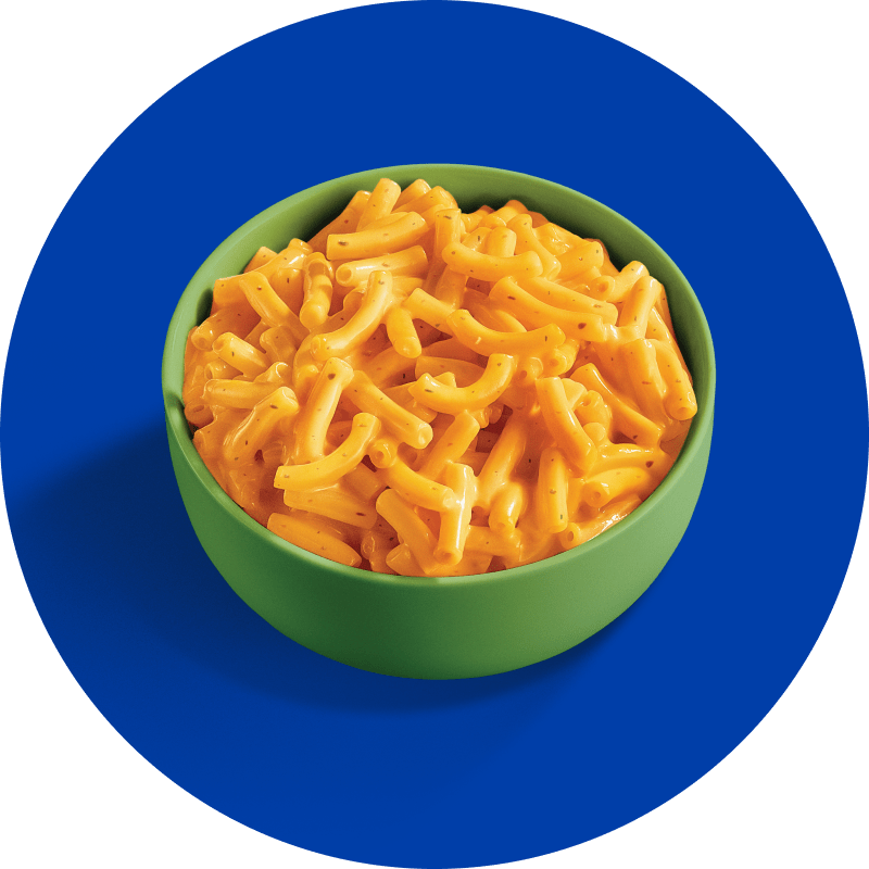 A vibrant, circular image showcasing a bright green bowl overflowing with creamy, orange-yellow macaroni and cheese. The background is a solid royal blue, and a subtle shadow is cast by the bowl on the blue surface.