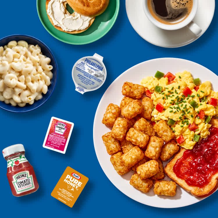 Breakfast spread with scrambled eggs, tater tots, and Kraft Heinz single-serve condiments on a blue background
